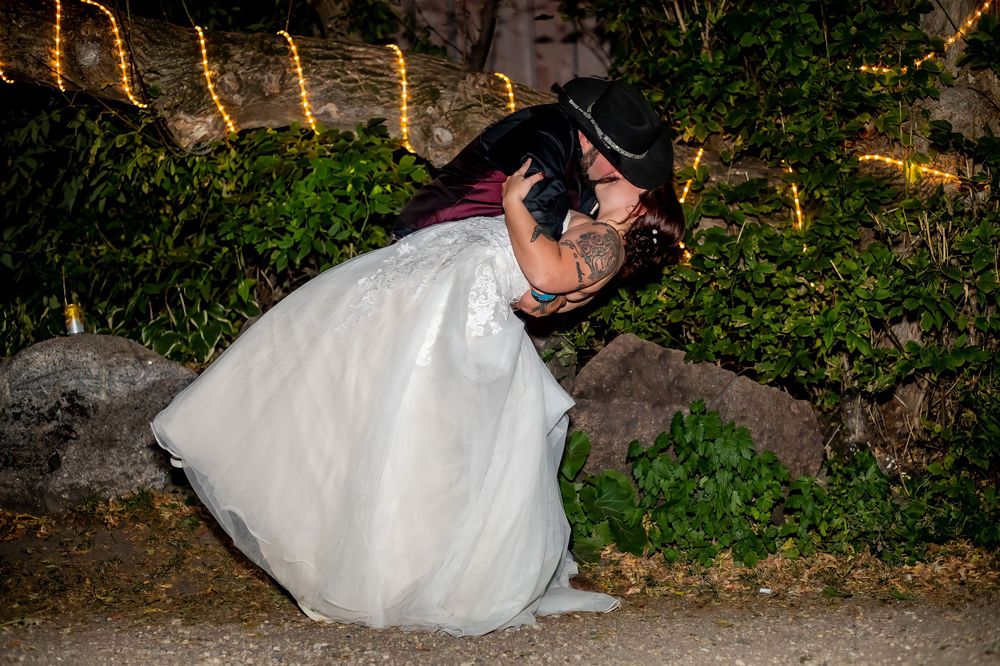 A romantic wedding photo of a couple sharing a kiss against a garden background with twinkling lights.