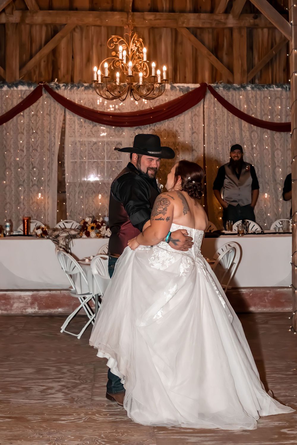 A romantic first dance in a rustic barn venue with twinkle lights and burgundy decorations.