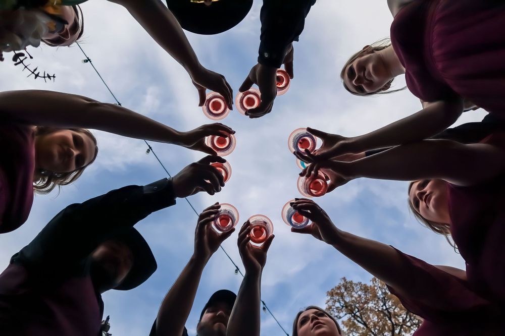 A creative wedding photo showing hands holding Coca-Cola bottles in a circular formation against a blue sky.