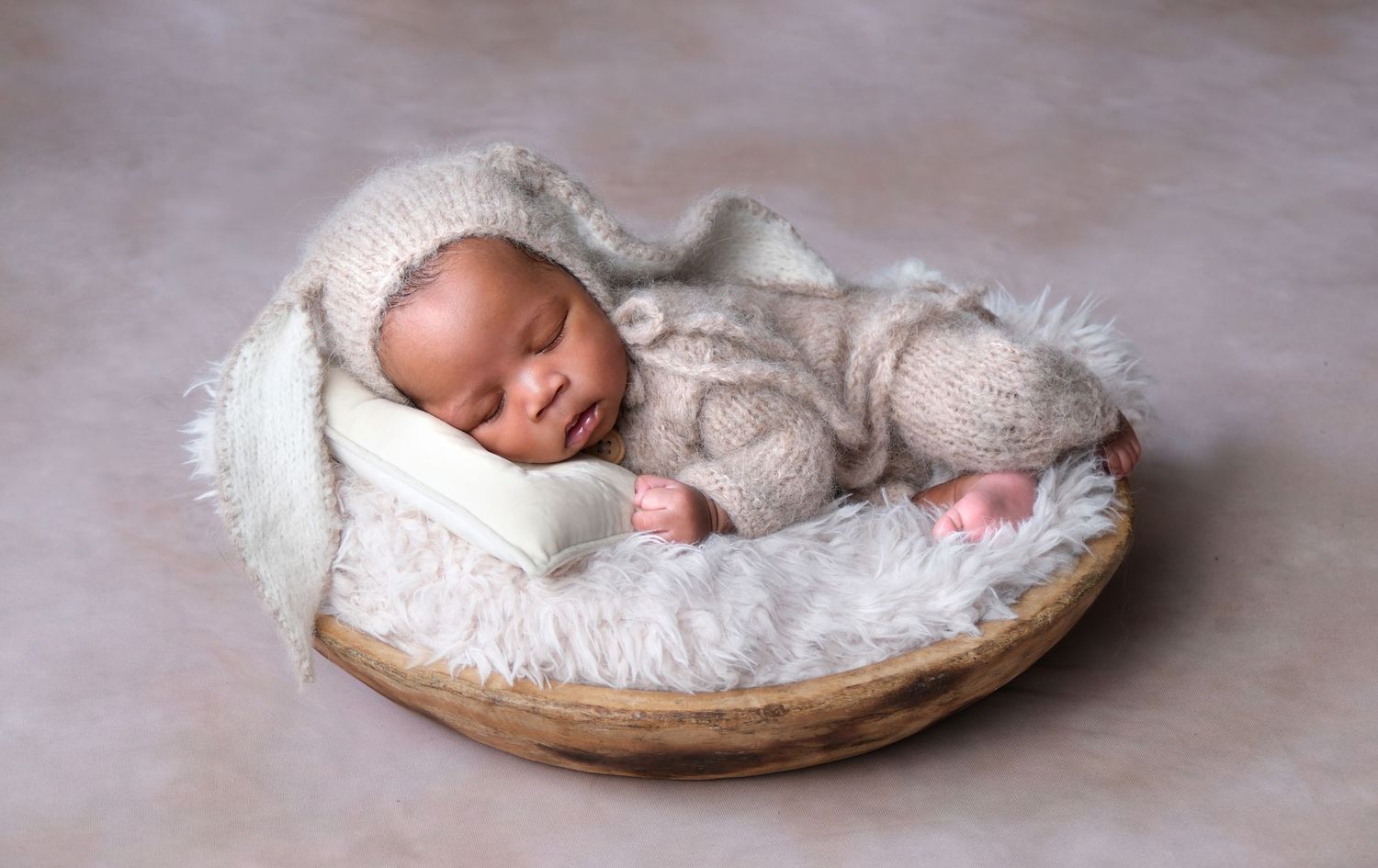 Baby posed in wooden bowl prop wearing cute bunny ears during newborn photography session