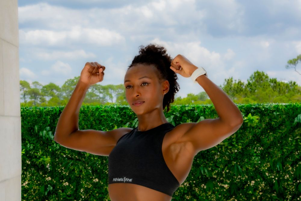 Athletic figure in black sports bra flexing against tropical greenery.