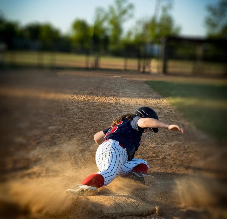 Baseball player slides dramatically into base creating dust cloud on baseball diamond.
