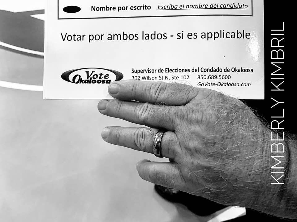 Close-up of hand with wedding ring pointing at voting instructions in Spanish.