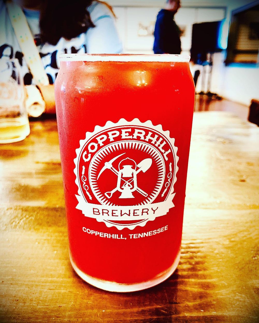 Red glass with Copperweld Brewery logo from Tennessee on wooden bar surface.