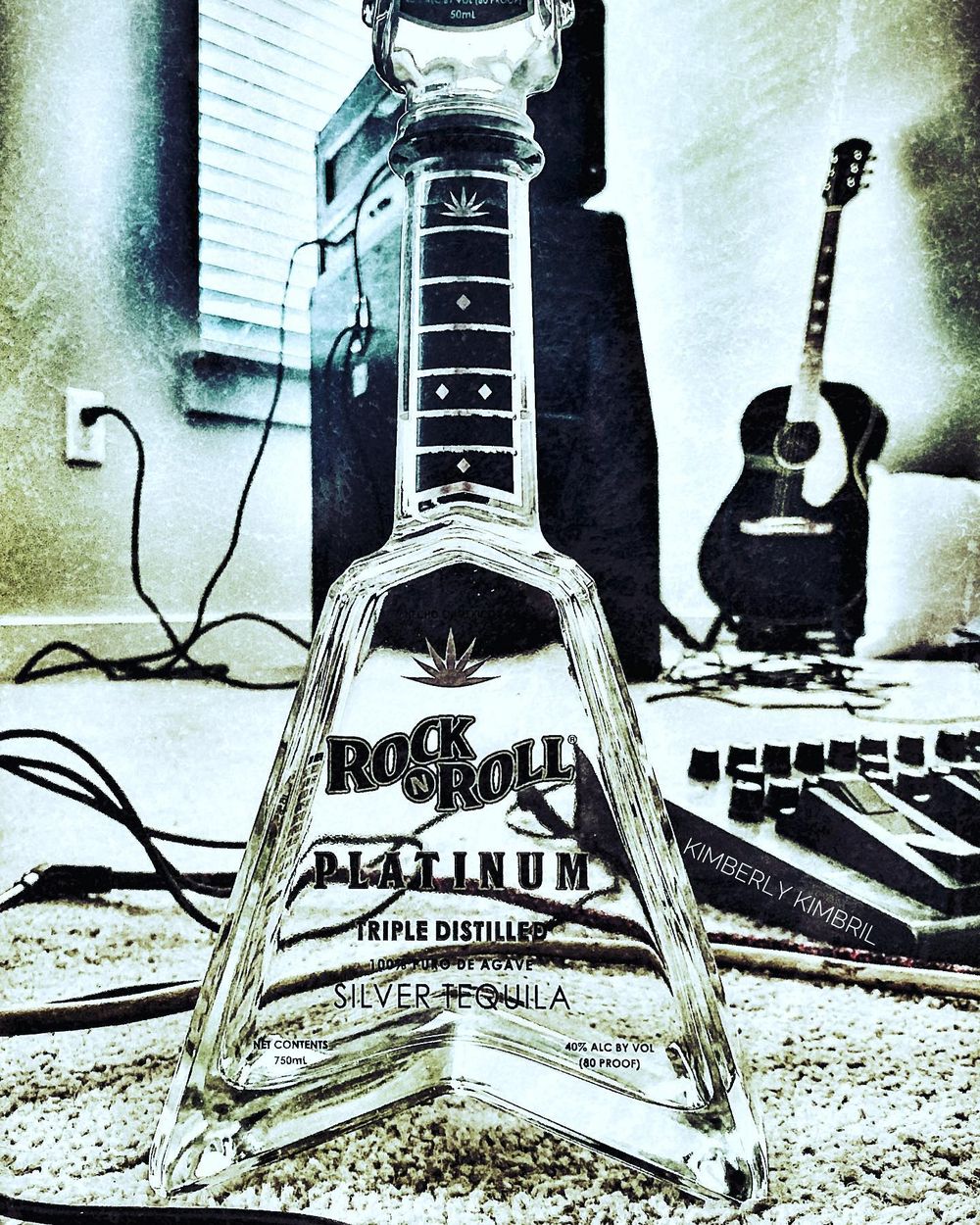 Rock and Roll Platinum tequila bottle displayed with guitars and music equipment in background.