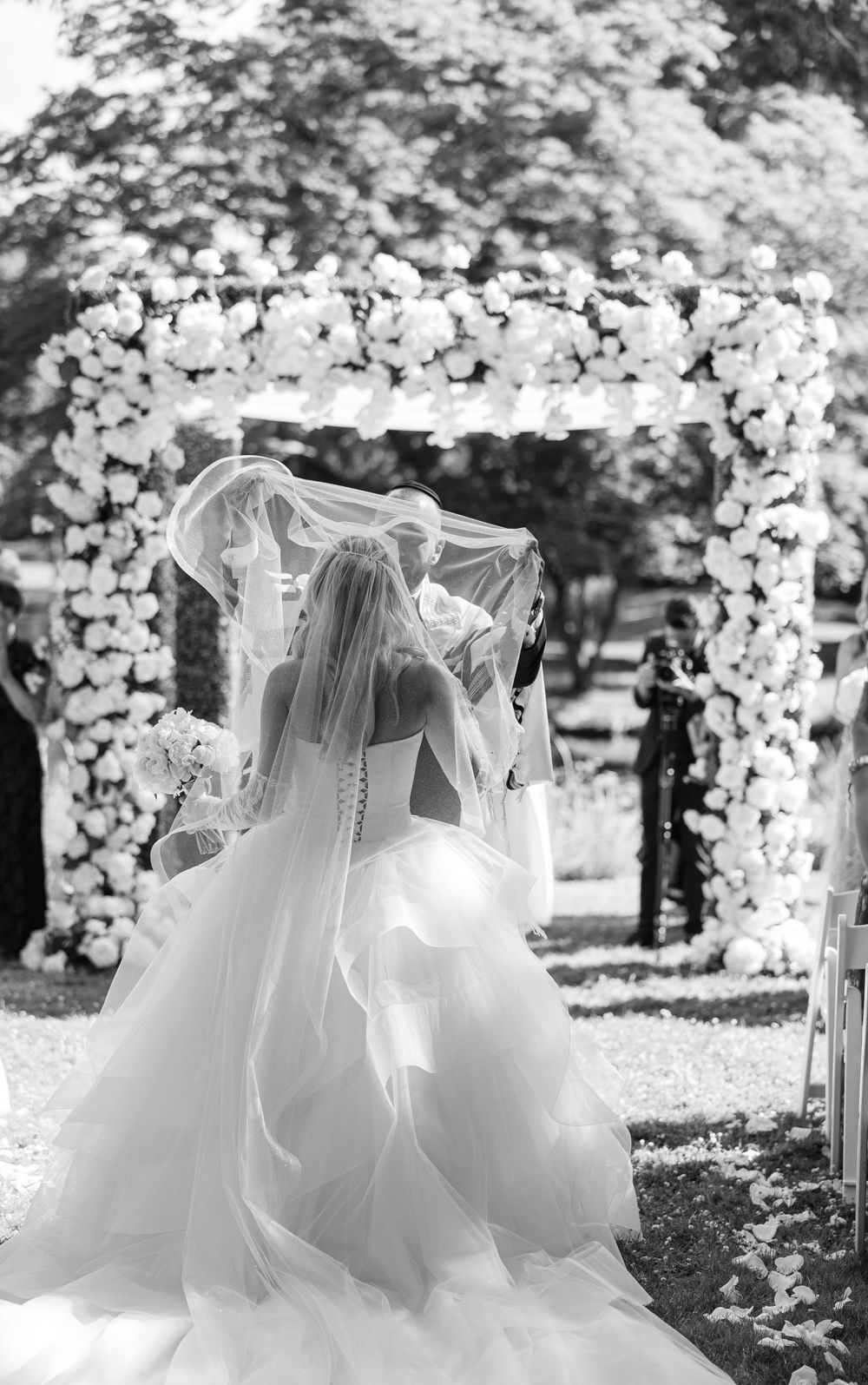White floral arch with flowing bridal gown and veil silhouetted in black and white.