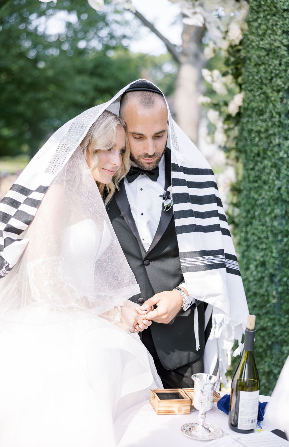 Intimate moment during Jewish wedding ceremony under traditional tallit prayer shawl.