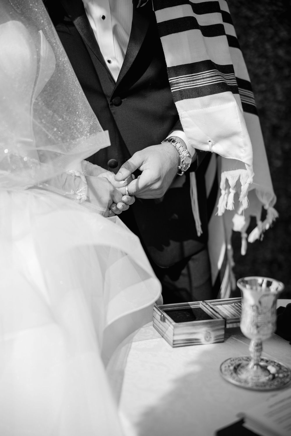 Close up of hands during Jewish wedding ceremony with traditional prayer shawl.