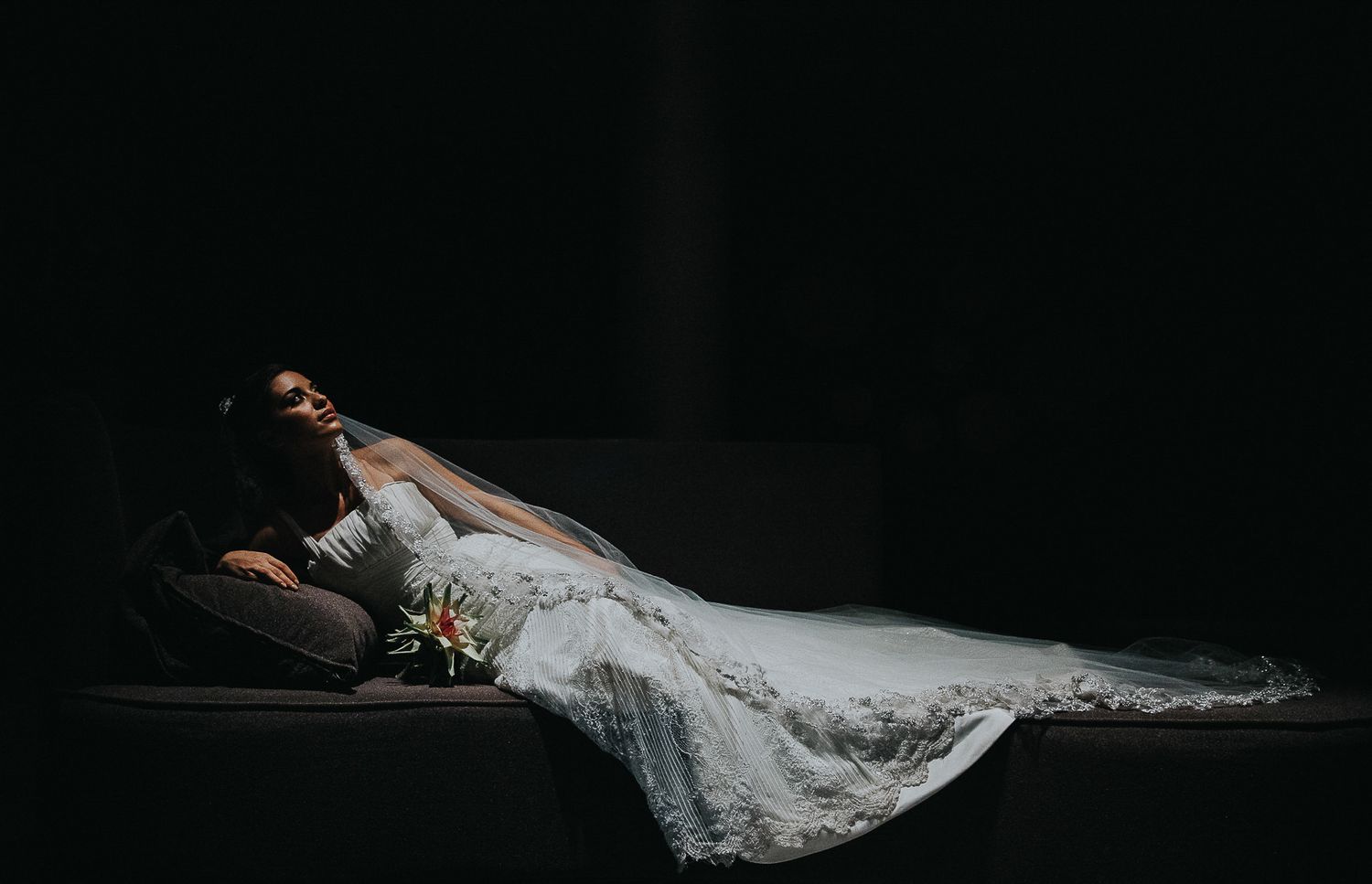 Dramatic bridal portrait with flowing white dress against dark background.