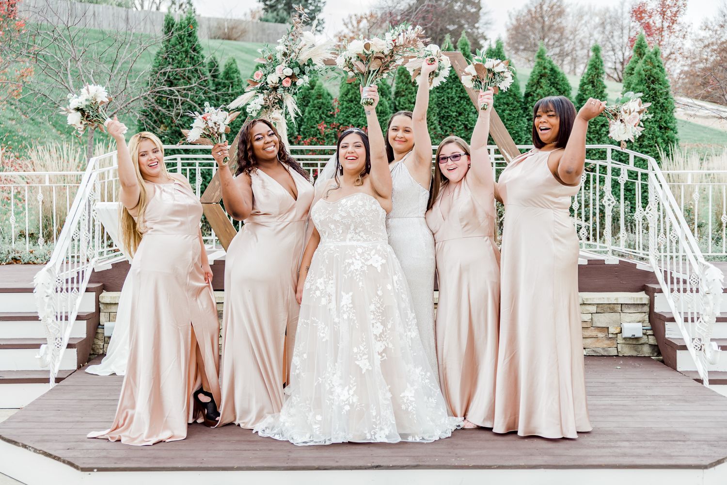 Wedding party in blush dresses celebrating on outdoor deck with joyful expressions by Stephanie Coulter Photography