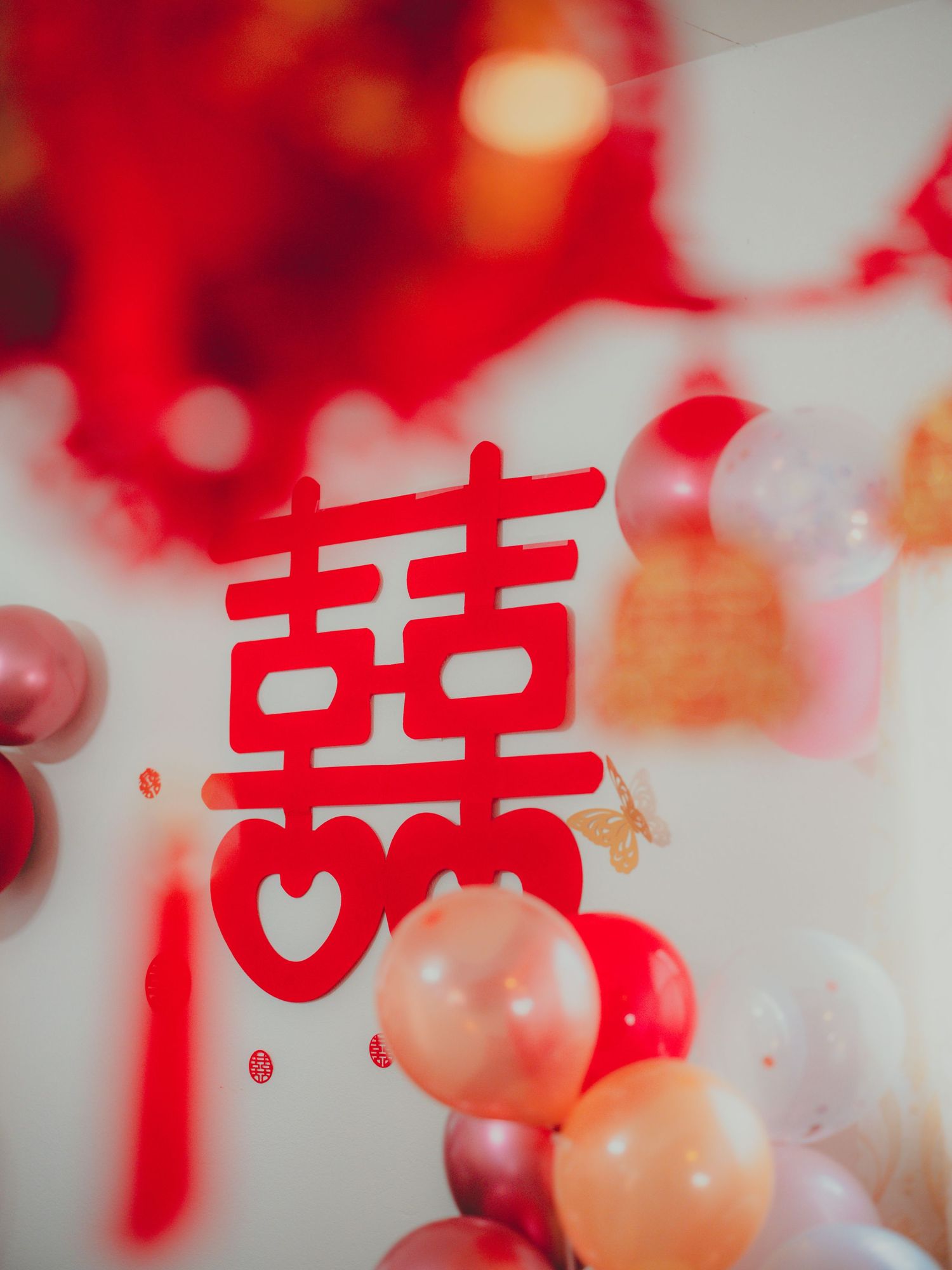 Traditional Chinese double happiness symbol in red surrounded by pink and red balloons.