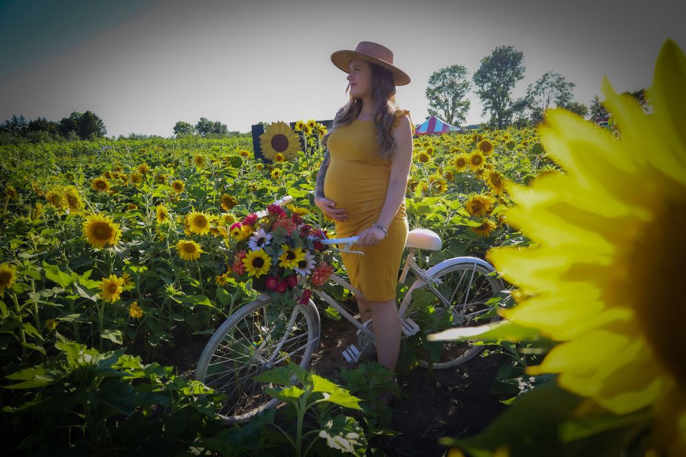 A figure with a bicycle poses among bright yellow sunflowers on a sunny day.