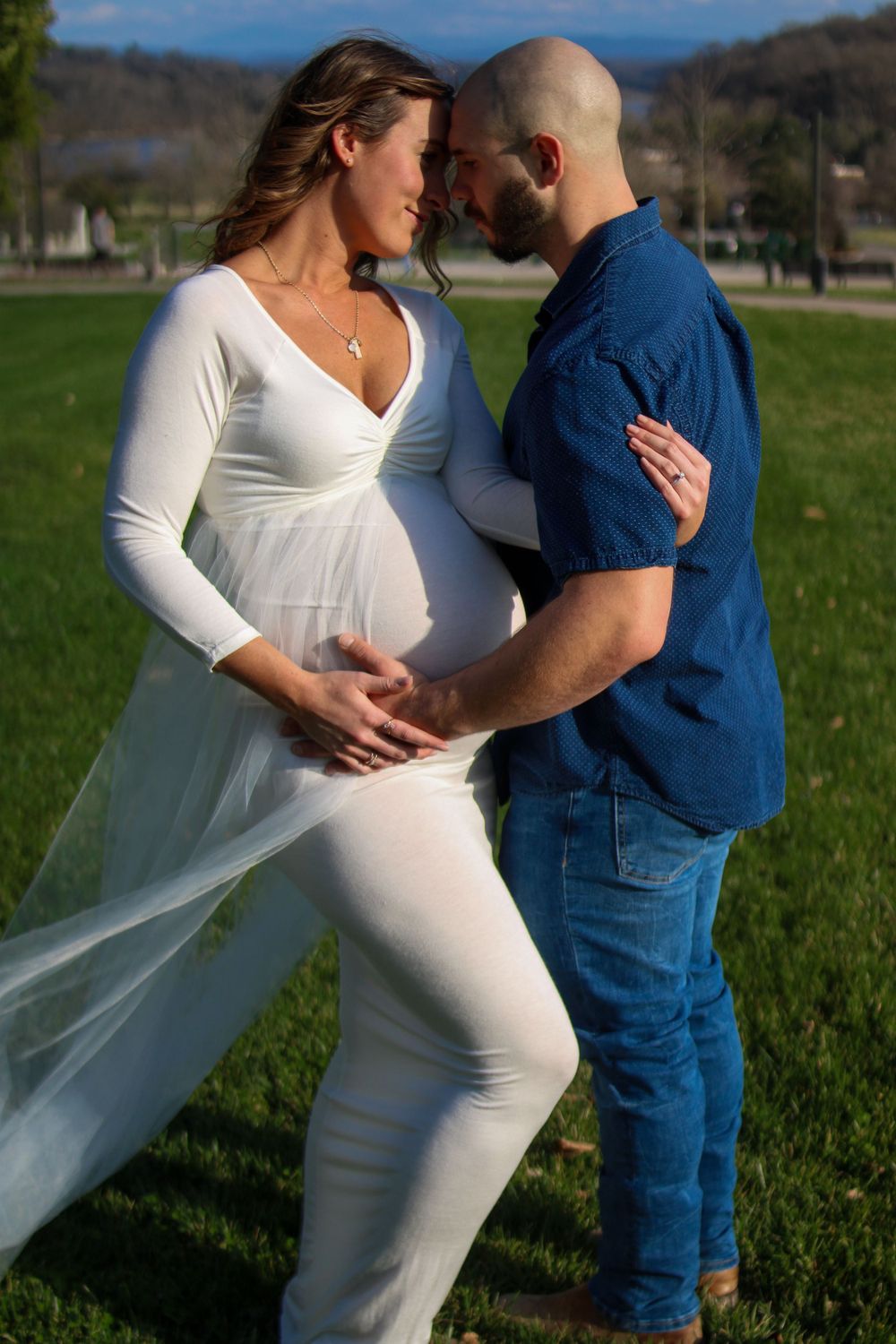 Couple poses together in a grassy field with mountains in background.