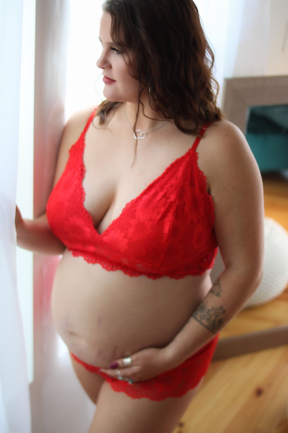 Woman in red lace lingerie poses against a white wall in natural light.