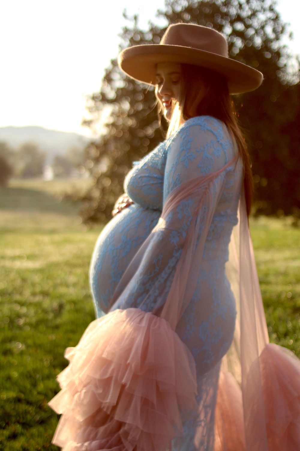 Maternity silhouette at sunset wearing flowing pink dress and wide-brim hat.