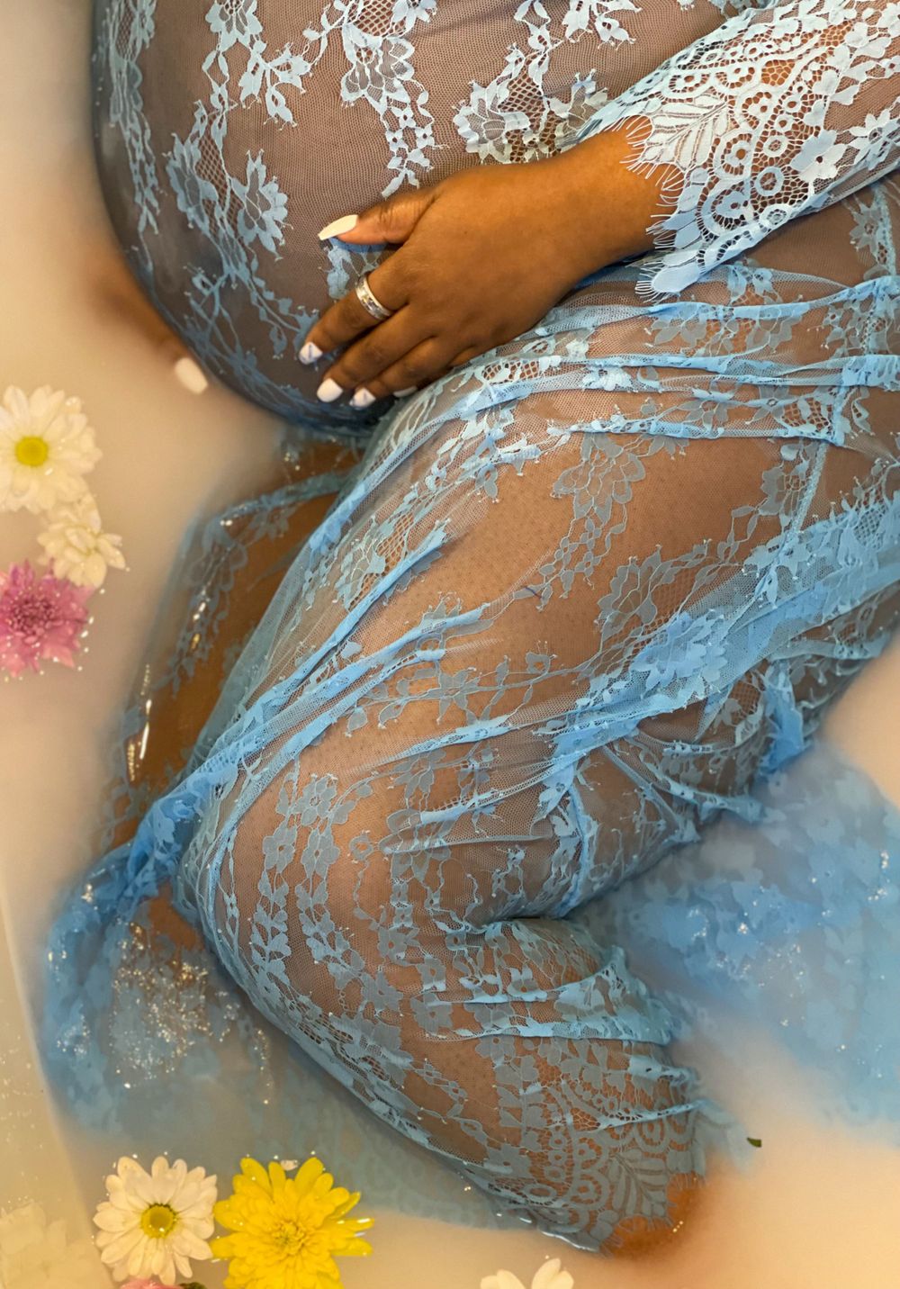A maternity photo with blue lace dress and yellow daisies in artistic composition.