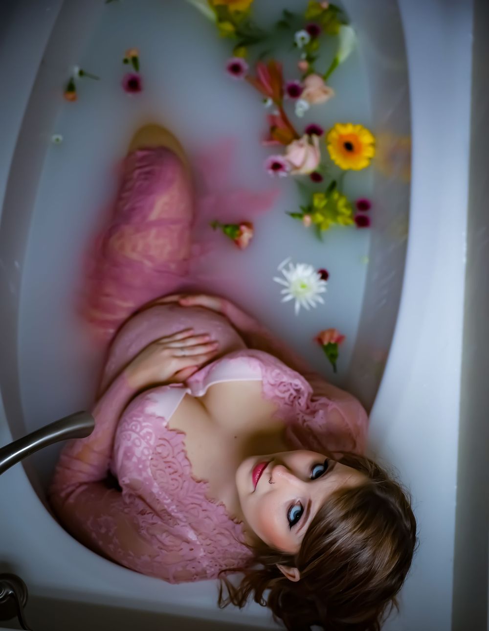 Artistic boudoir photo with pink lace and flowers in bathtub setting.
