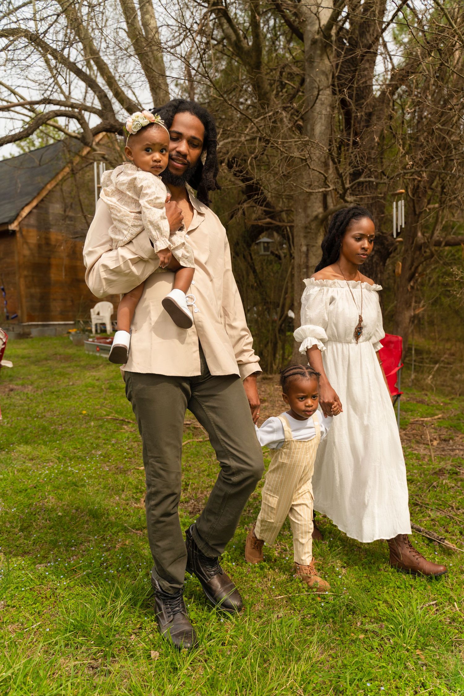 A family stands together on grassy ground near trees with a rustic cabin in the background.