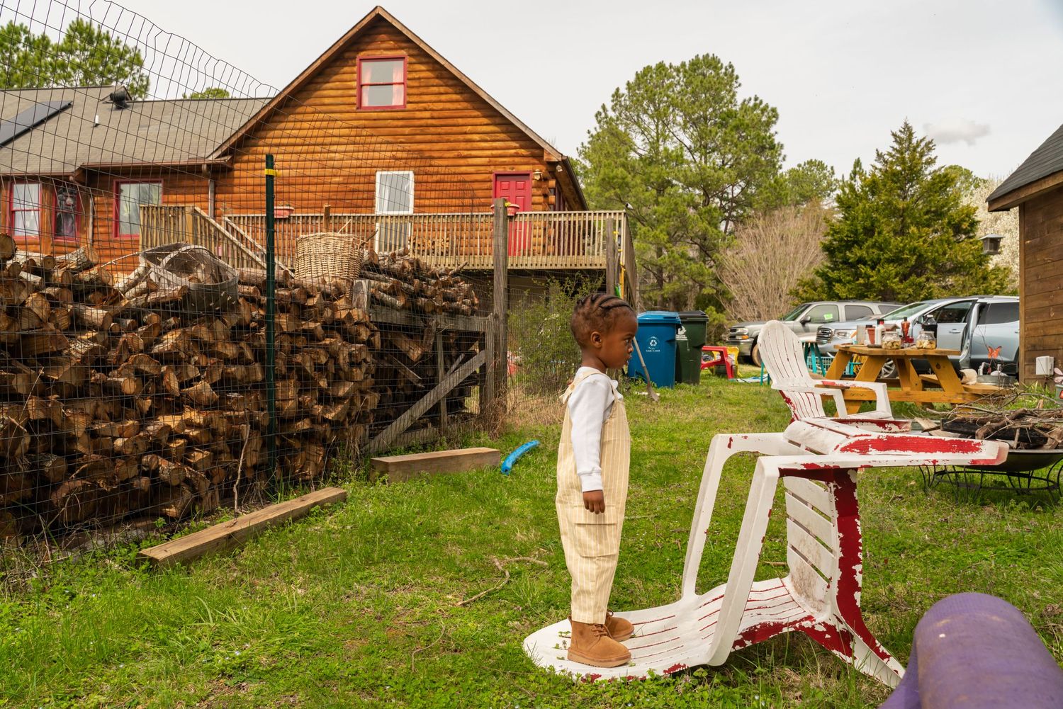 A rustic log cabin with a deck sits among trees with yard items visible.