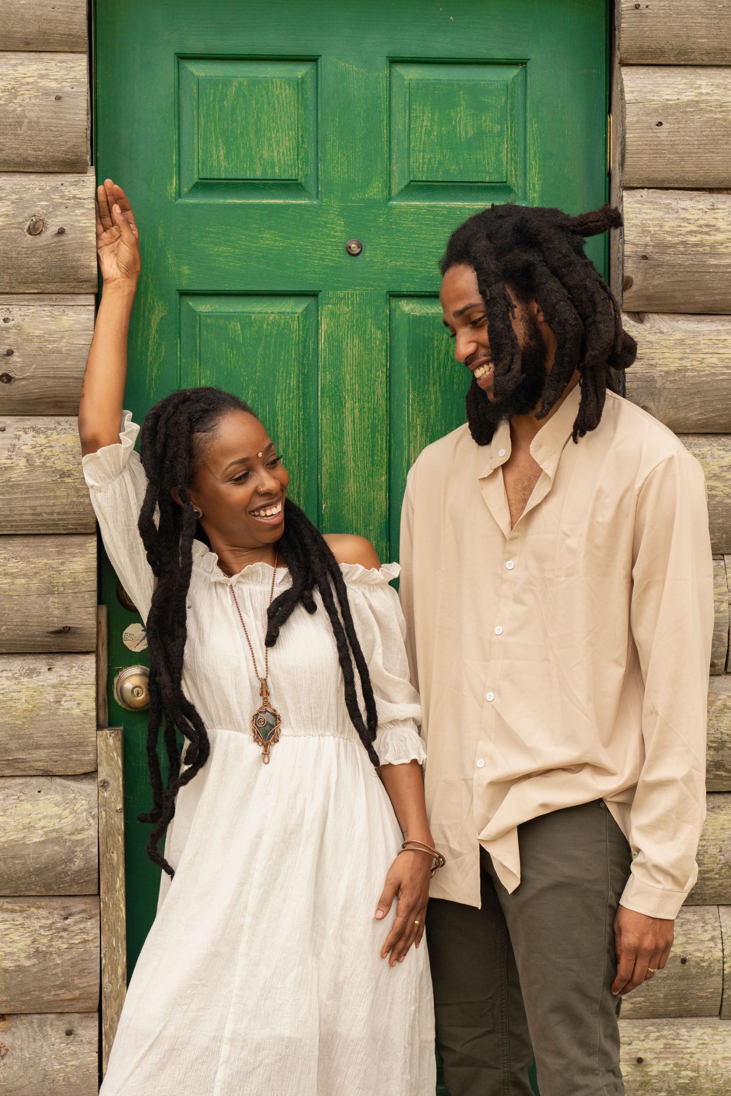 A couple shares a happy moment in front of a green door on a log cabin.