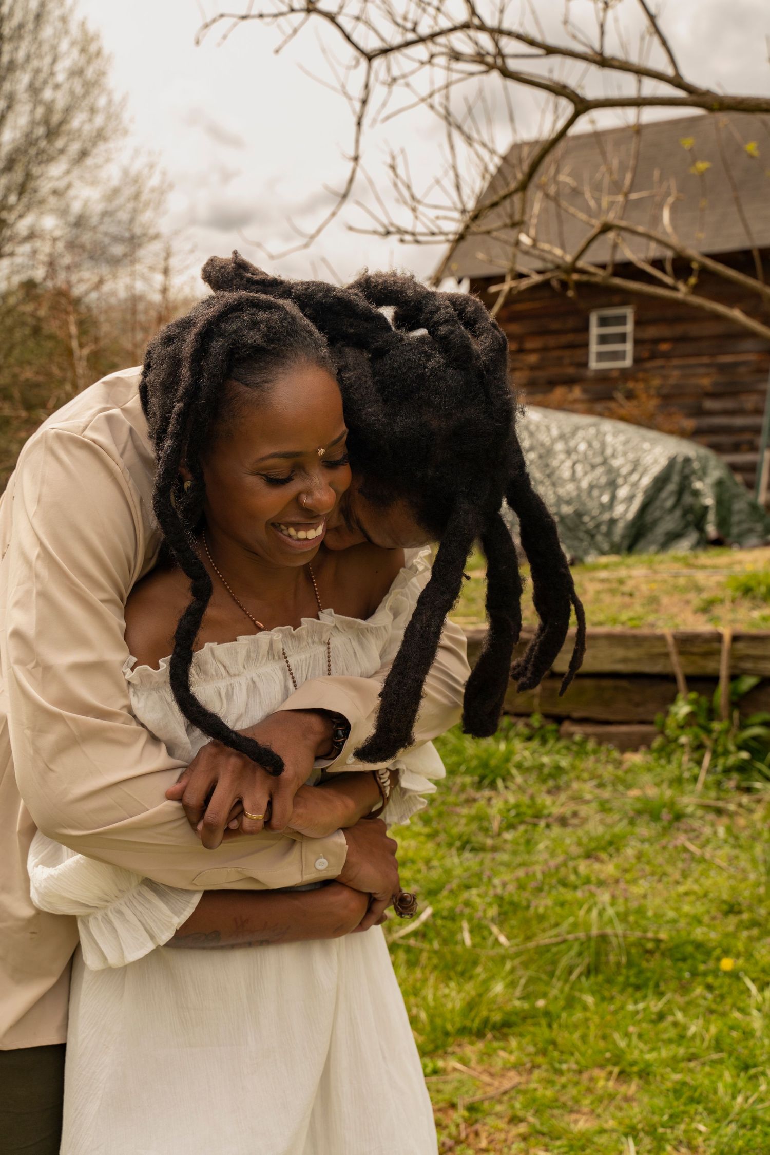 A joyful moment shared in an outdoor setting wearing white clothing near a rustic building.