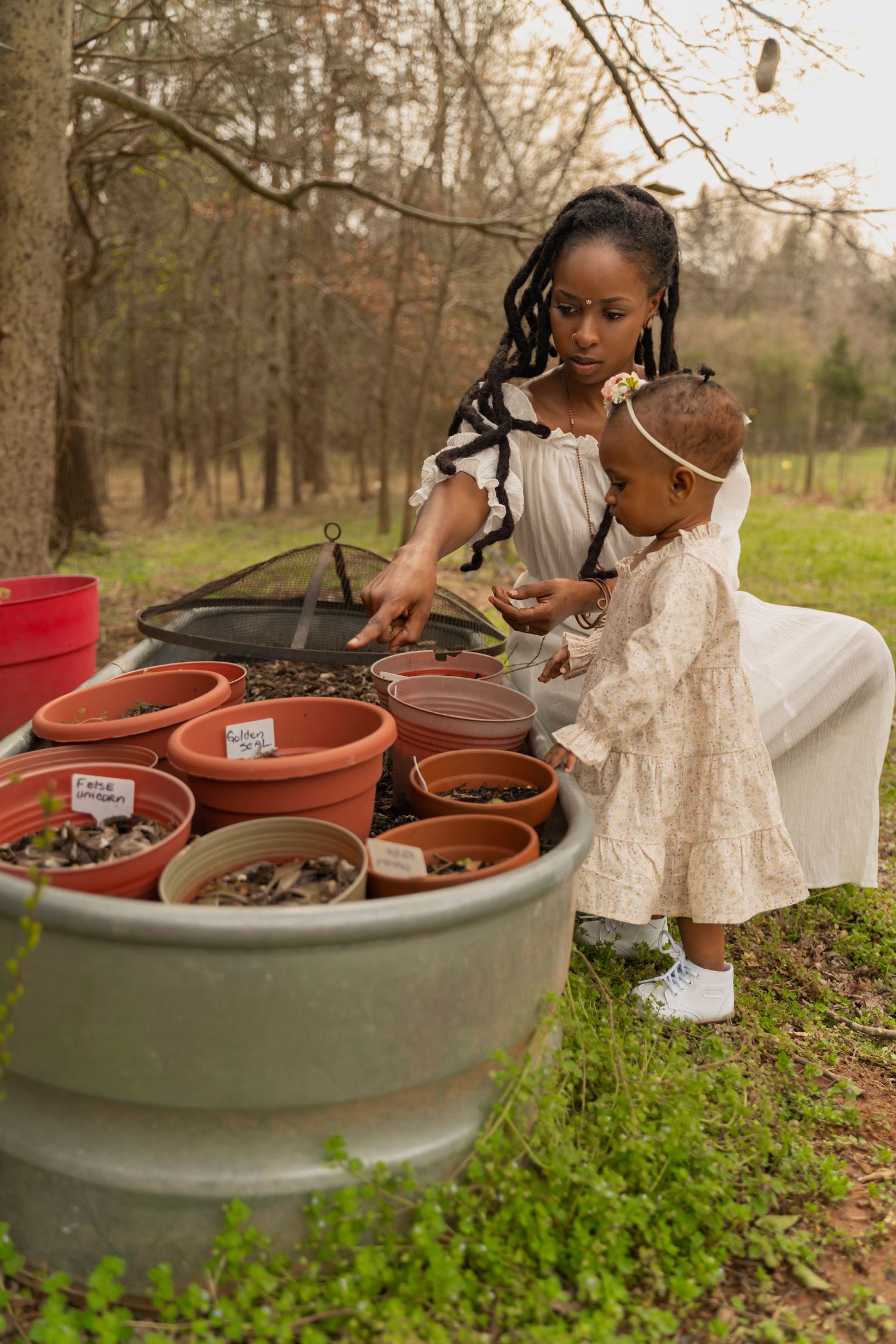A parent and child explore plant containers in an outdoor garden setting.