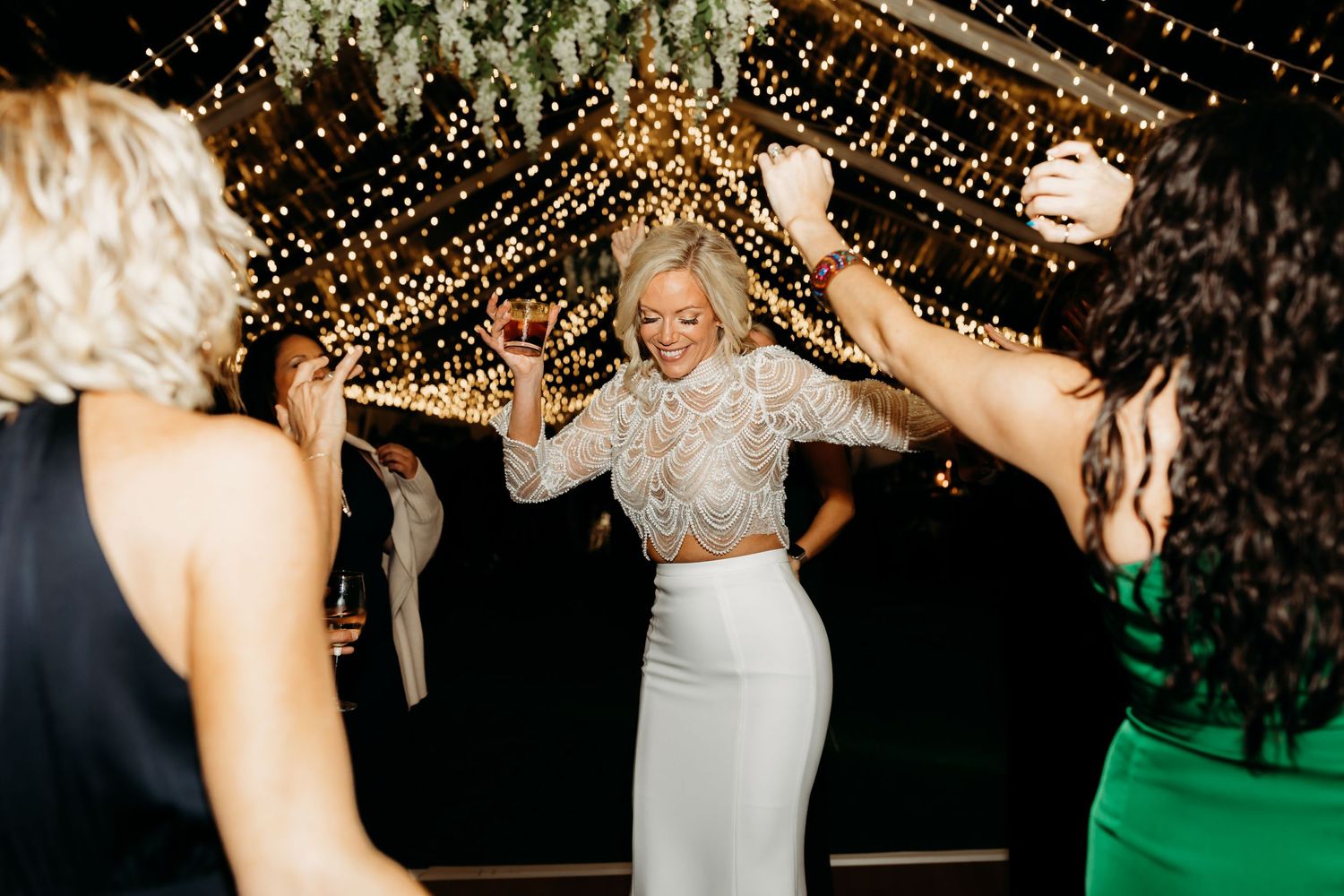Bride dancing joyfully with guests under string lights at a romantic outdoor wedding reception.