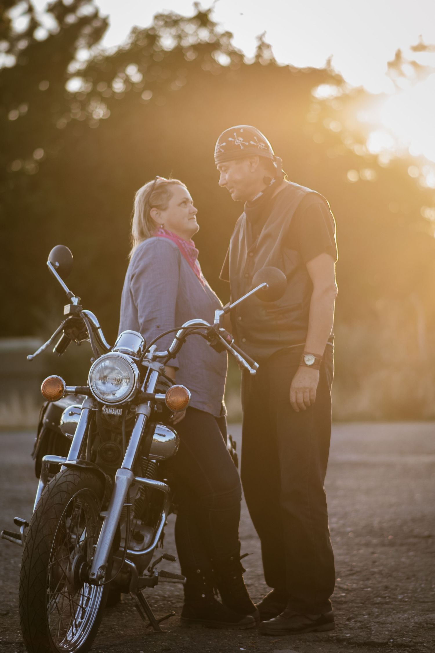 Sunset portrait of two people having a conversation next to a parked motorcycle.