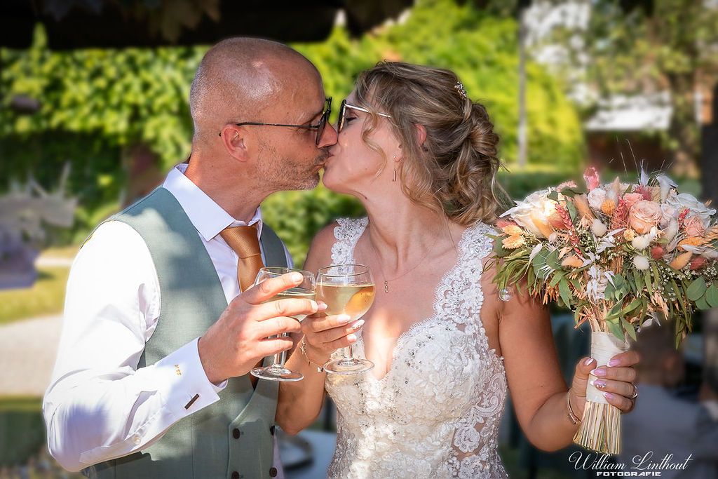 Newlyweds sharing champagne toast with bouquet in garden setting.