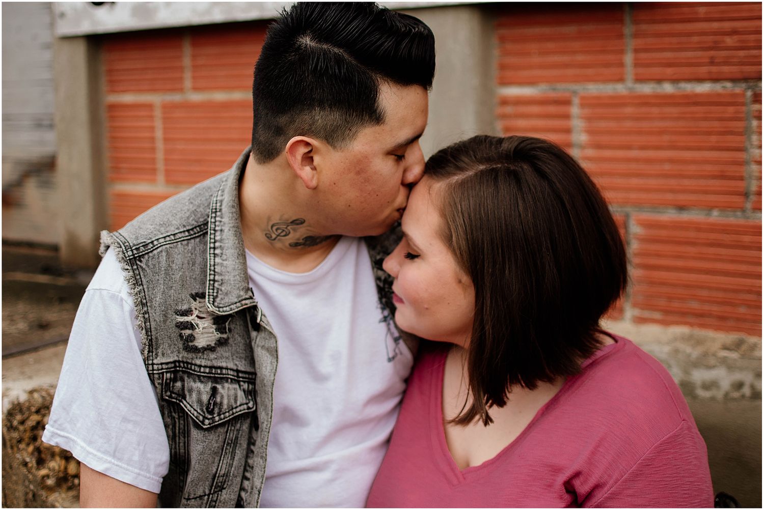 A tender moment shared between a couple against a brick wall backdrop.
