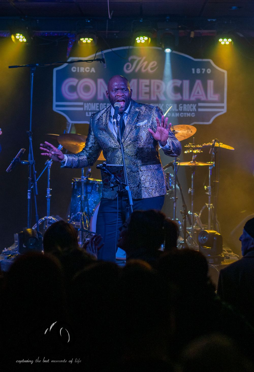 A performer in a shimmering jacket energetically entertains on stage at the Continental Club with dramatic lighting effects.