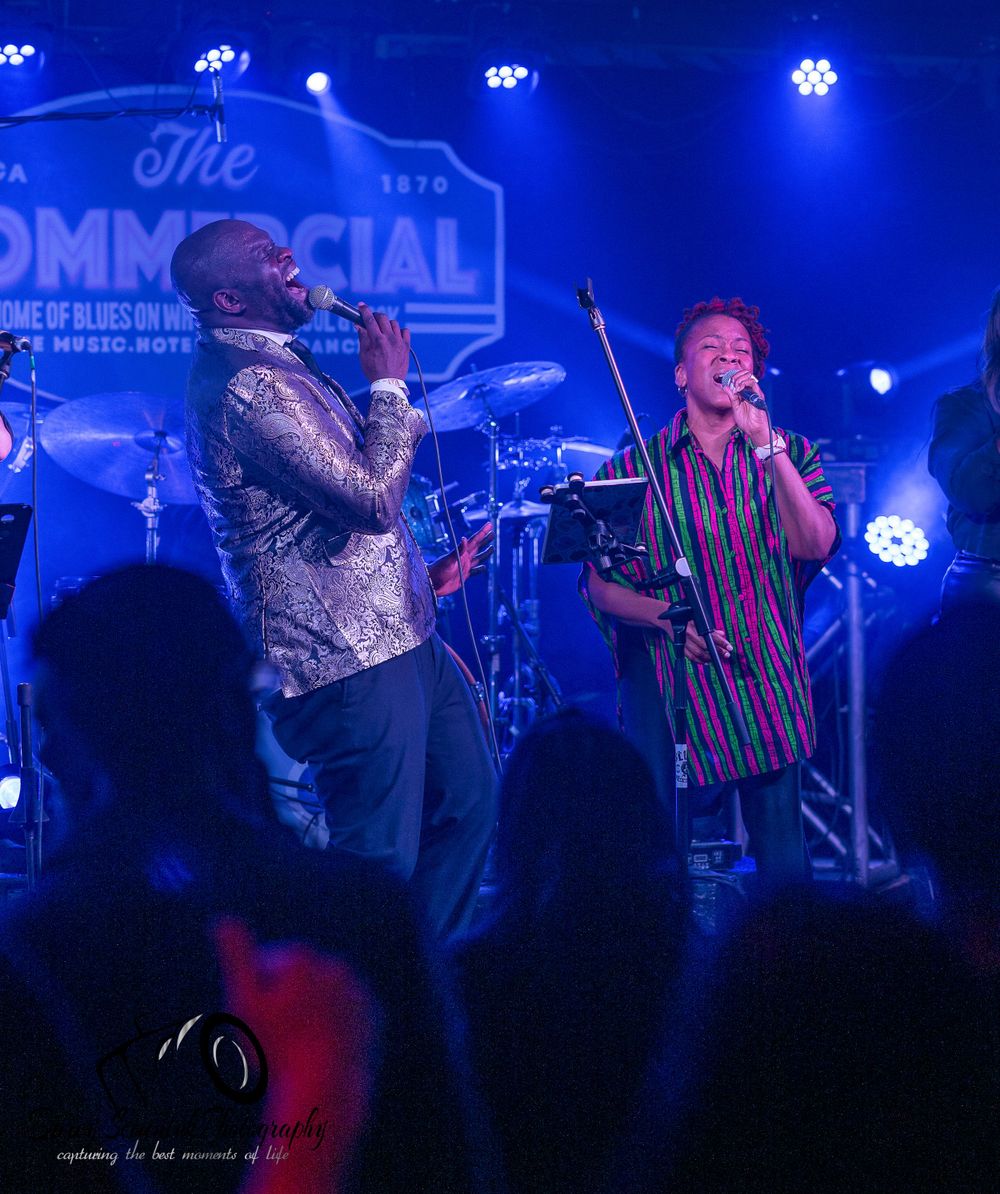 Concert performers on stage bathed in blue lighting during an energetic live music performance.