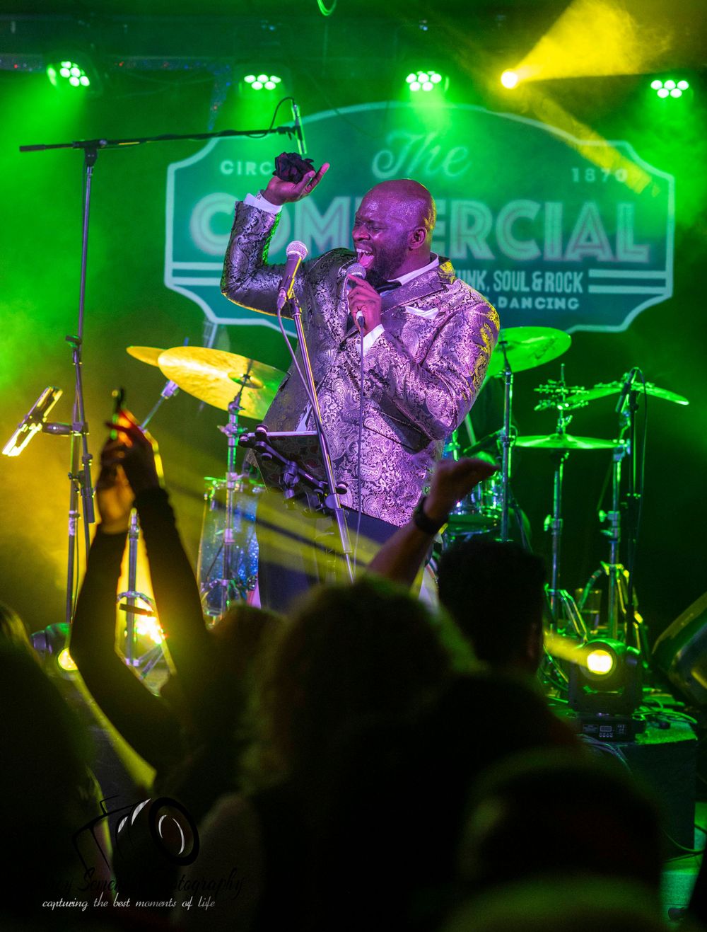 Concert performers on stage bathed in vibrant green and yellow lighting create an energetic atmosphere during live show.