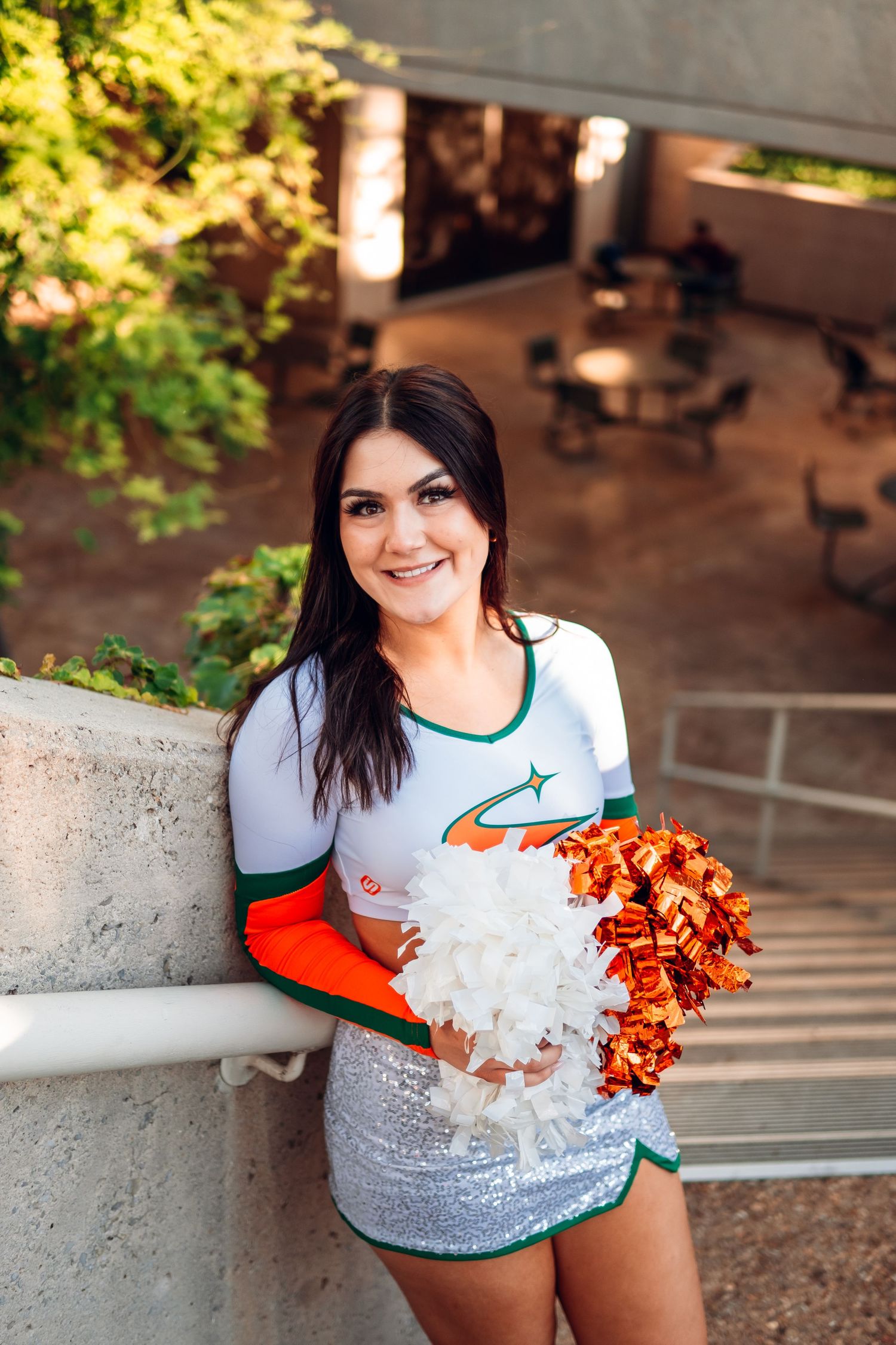 Cheerleader in white and orange uniform poses on campus steps.