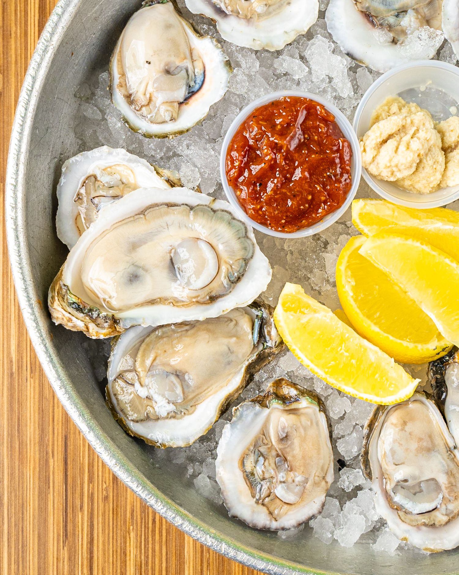 Fresh oysters on ice served with cocktail sauce, lemon wedges and condiments in a round platter.