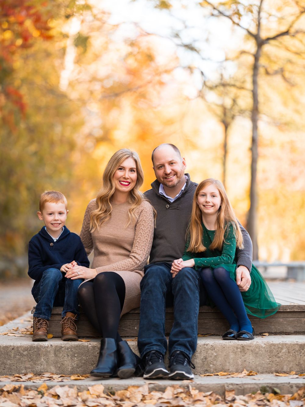 Family sitting together outdoors in an autumn setting, smiling warmly. Toronto family photography.