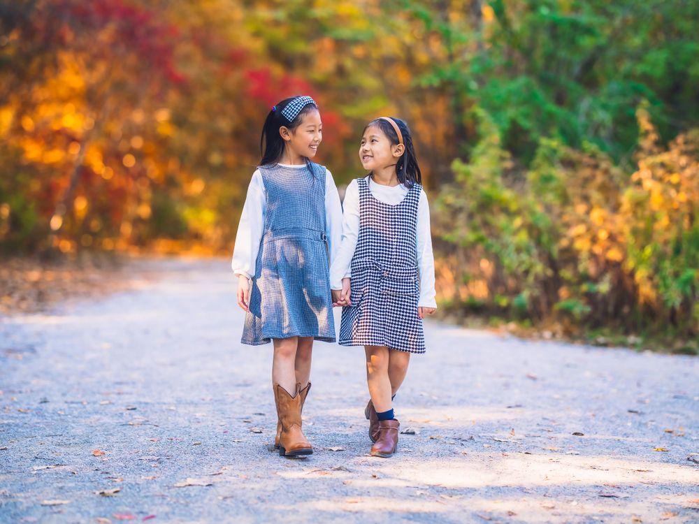 Two young girls in vintage-style dresses walking hand in hand on a scenic path. Toronto family photography.