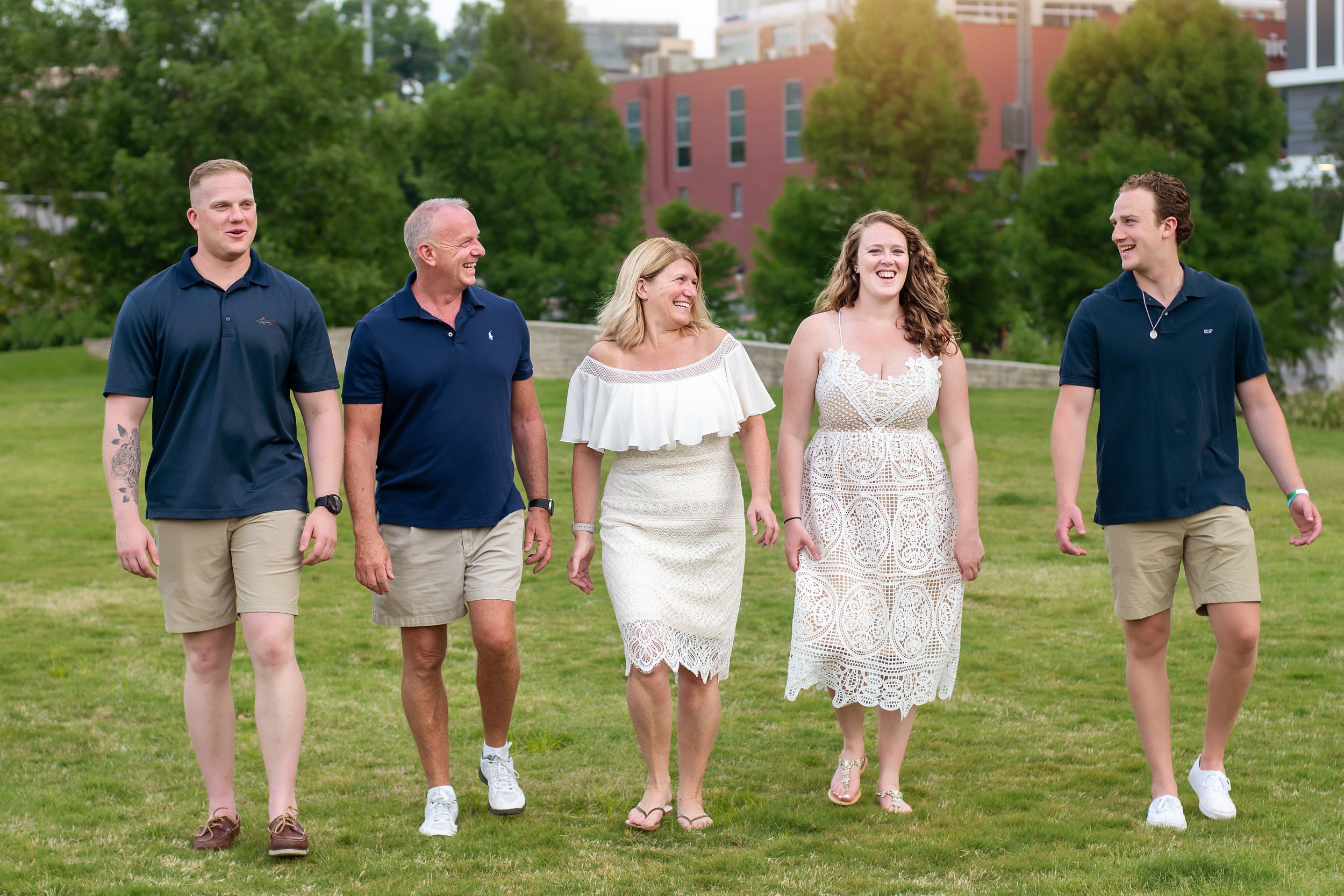 Family group walking and posing casually on green grass with brick buildings in background.