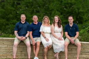 Family members sitting relaxed on stone wall outdoors wearing coordinated navy and white outfits.