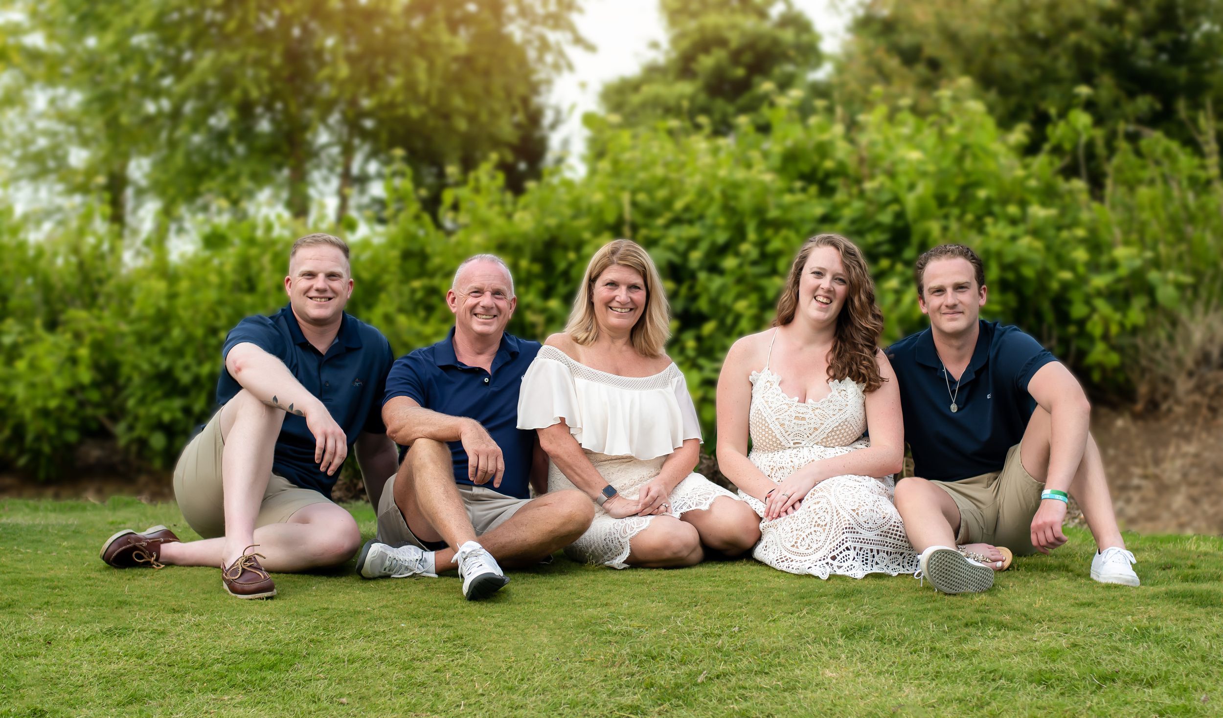 Family portrait series showing casual poses on grass with stone wall background.