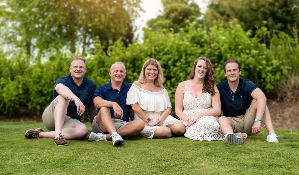 Family portrait series showing casual poses on grass with stone wall background.