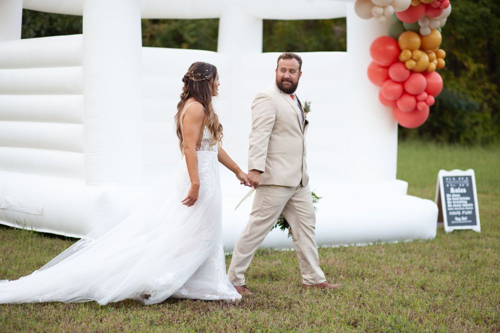 A bride and groom walk in front of a bounce house with balloons at the House on Barber Mill in Clayton, NC.