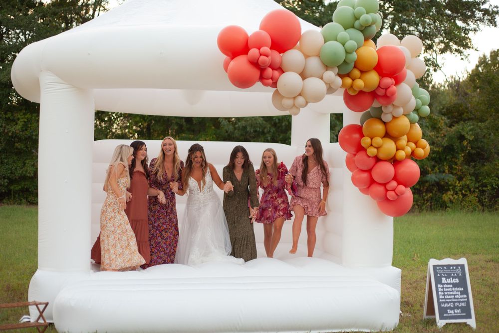 A bride and bridesmaids jump on bounce house with balloons at the House on Barber Mill in Clayton, NC.