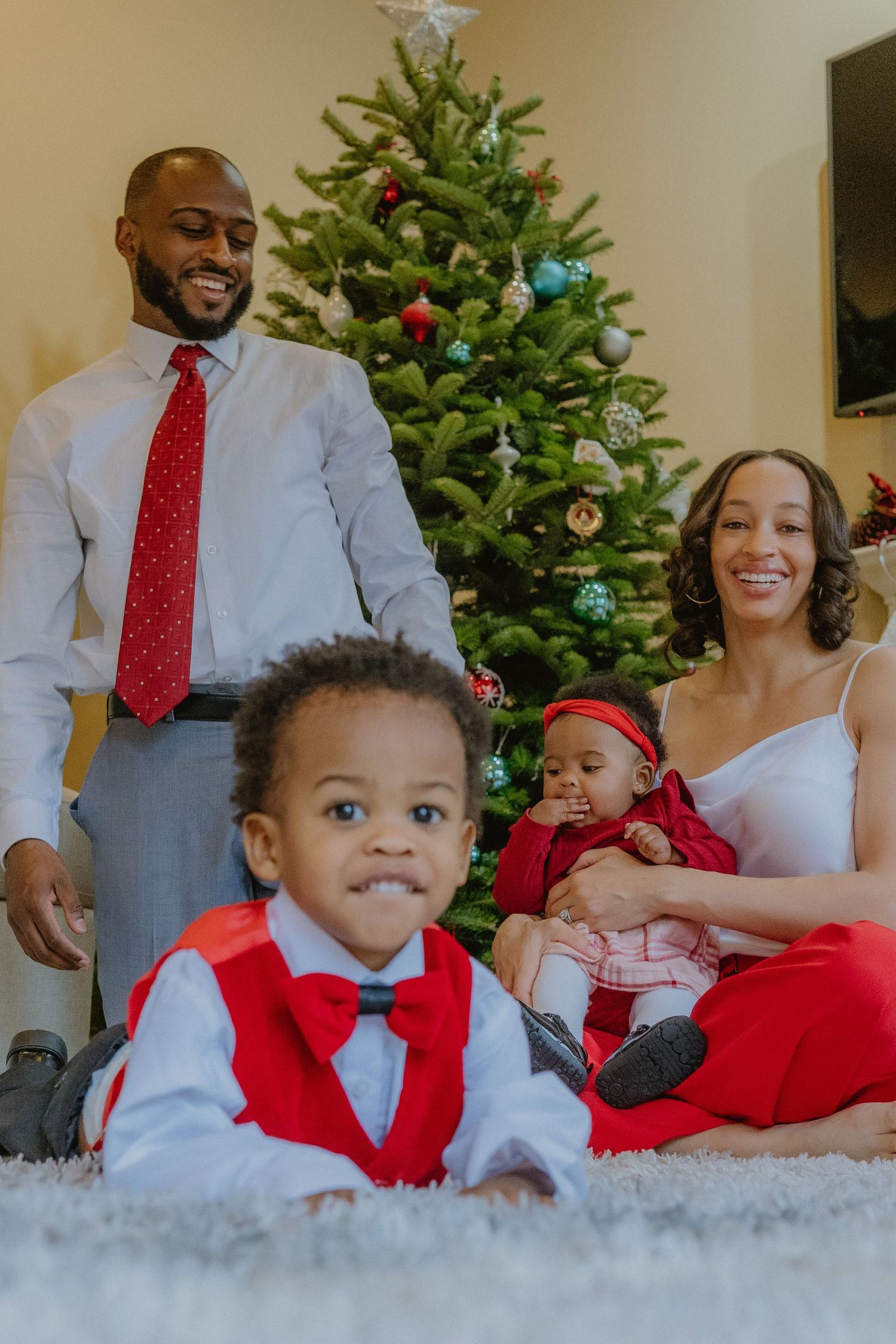 Family in festive attire posing by decorated Christmas tree in living room.