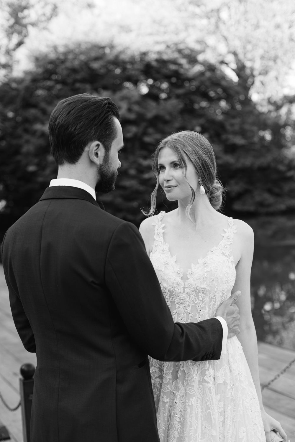 Black and white wedding portrait showing couple in elegant attire against natural outdoor setting.
