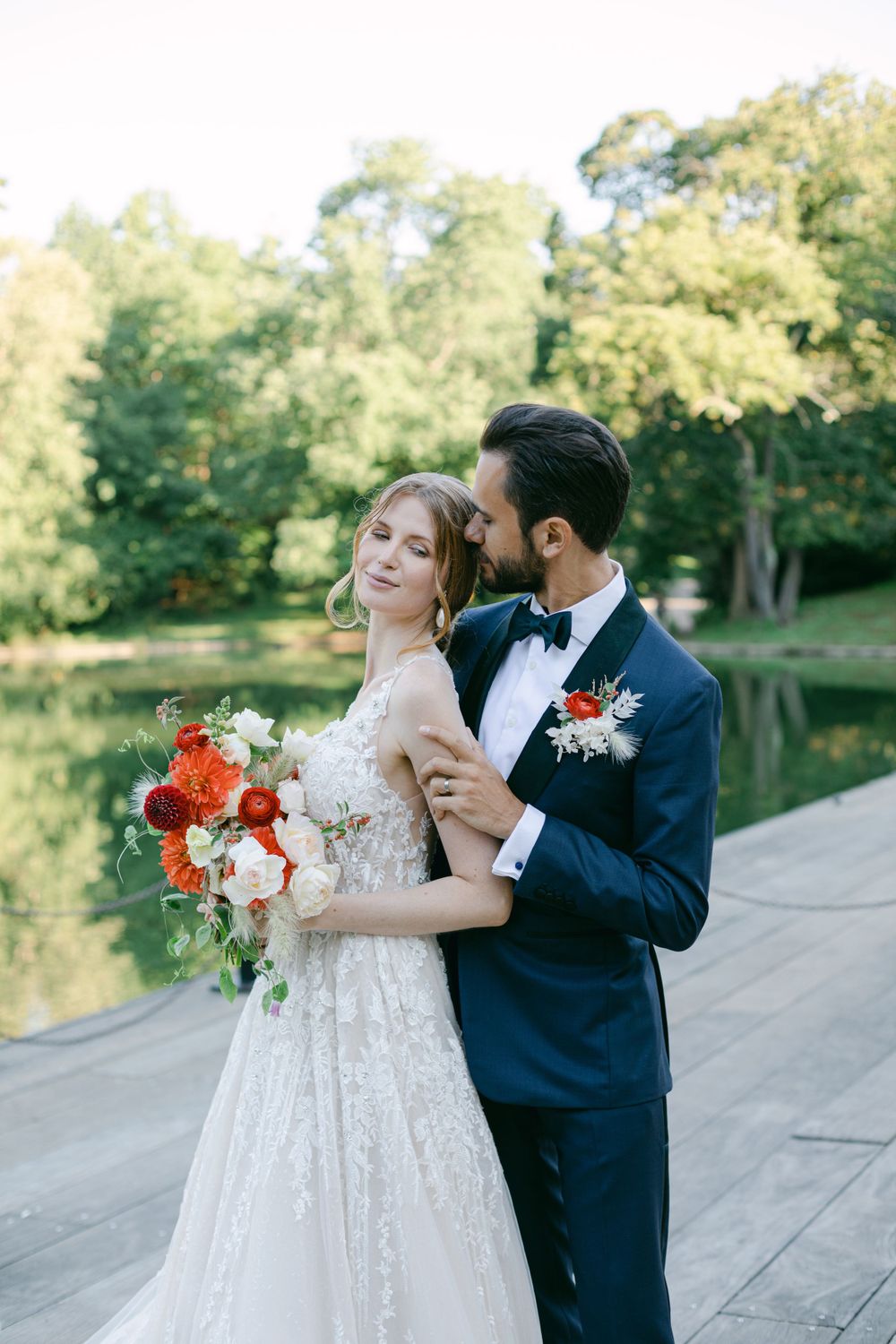 Romantic wedding portrait with couple holding vibrant orange bouquet in garden setting.