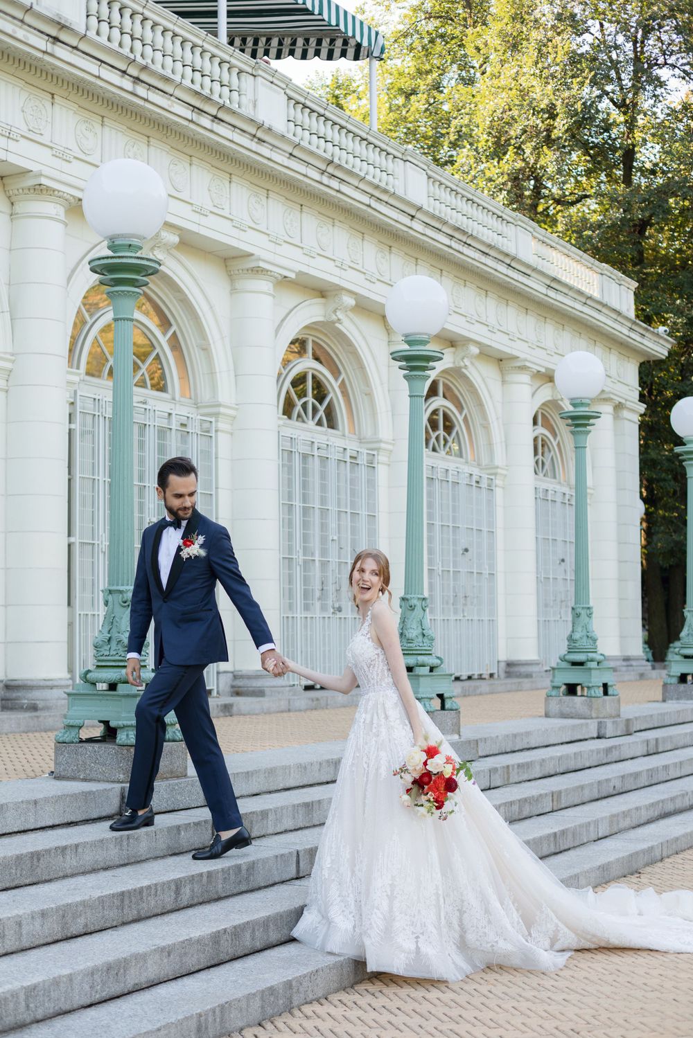 A newlywed pair descends elegant stone steps at a historic venue with mint green columns.