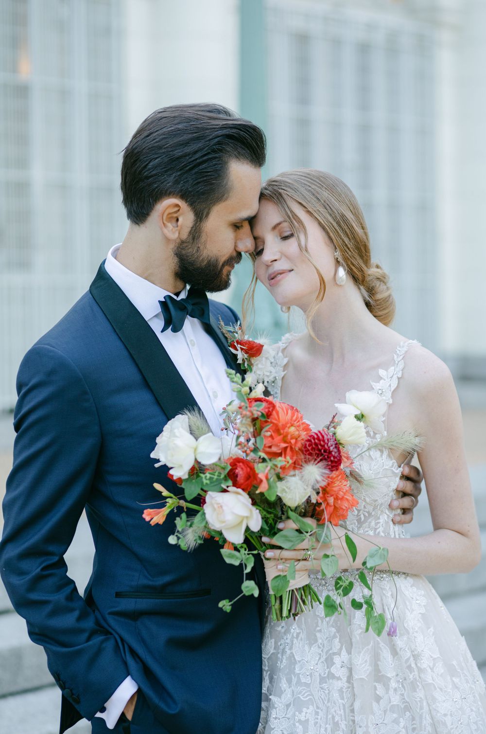 A tender wedding moment captured with coral and white florals against classic architecture.