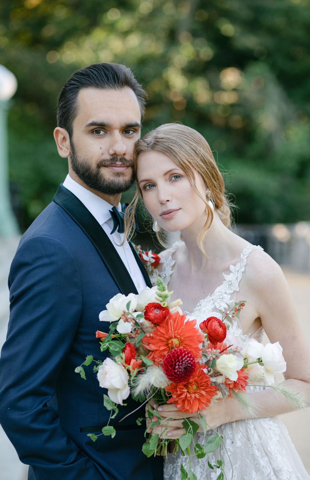 Wedding couple poses with vibrant coral and white floral bouquet against garden backdrop.