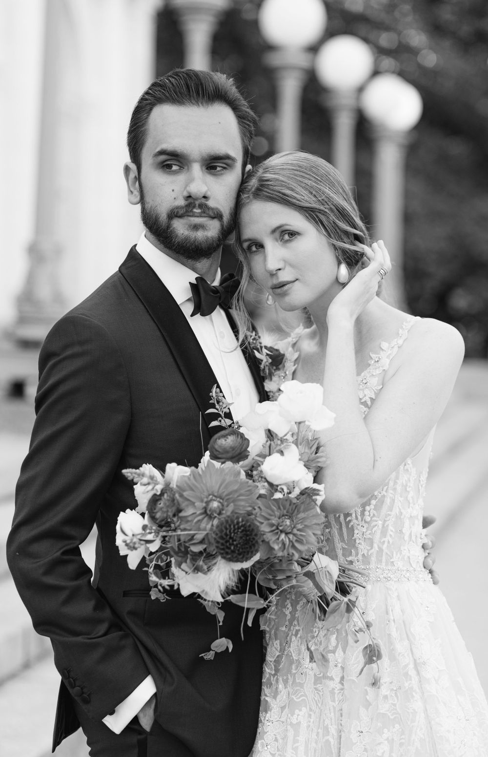 Classic black and white wedding portrait with couple holding floral bouquet against columned backdrop.